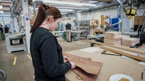 Eine Auszubildende arbeitet in der Holzwerkstatt an einem Holzfurnier.