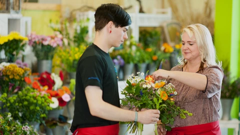 Ein Auszubildender und eine Ausbilderin binden einen Blumenstrauß.