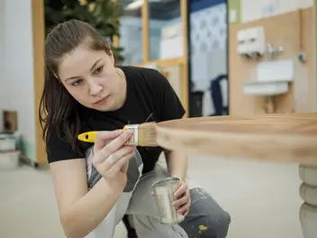  Eine Auszubildende lackiert einen Holztisch.