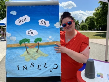 Lydia Motz steht neben einem bunten, selbstgemalten Plakat mit der Aufschrift "Reif für die Insel?"
