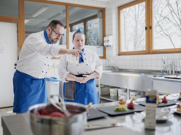 Ein Ausbilder erklärt einer Auzubildenden etwas in der Küche.
