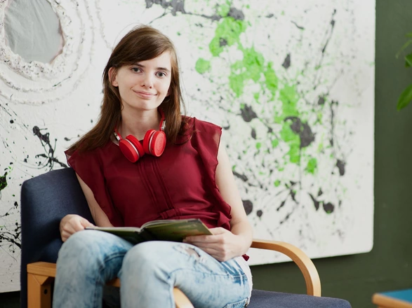 Eine Jugendliche sitzt mit einem Buch auf einem Sessel.