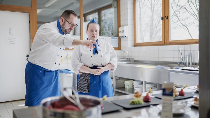 Ein Ausbilder erklärt einer Auzubildenden etwas in der Küche.