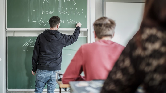 Lehrer schreibt etwas an die Tafel.