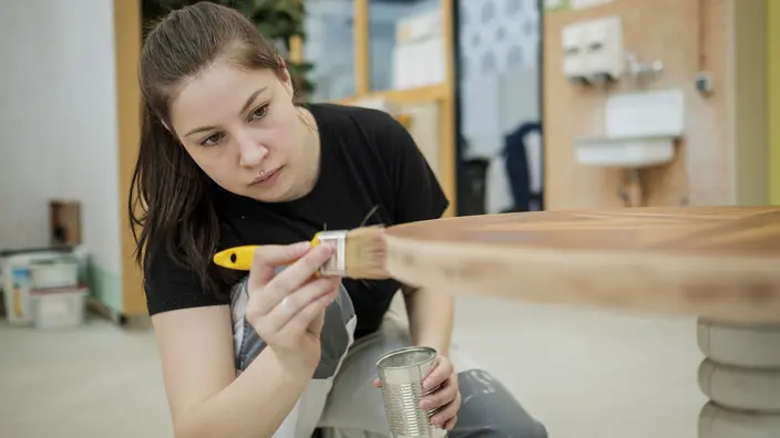  Eine Auszubildende lackiert einen Holztisch.