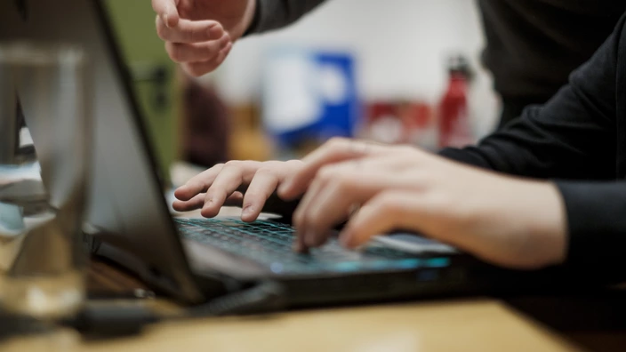 Nahaufnahme von einem Laptop und mehreren Händen.