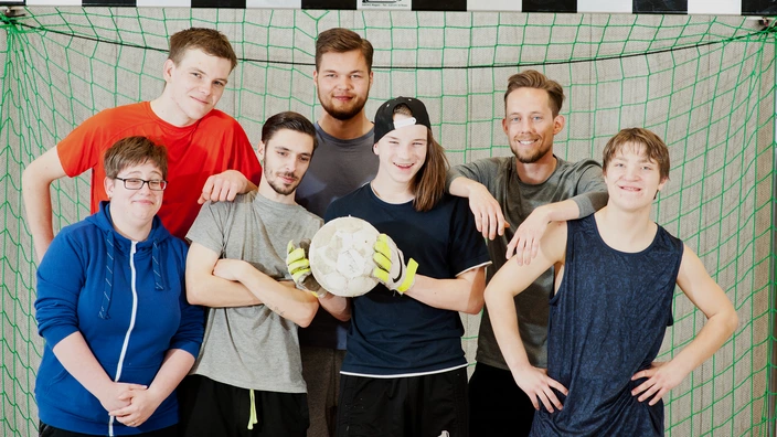 Gruppenfoto von sieben Personen vor einem Fußballtor.
