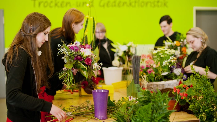 Fünf Auszubildende binden Blumensträuße im Floristikbereich.