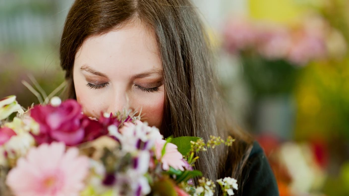 Eine Auszubildende riecht an einem Blumenstrauß.