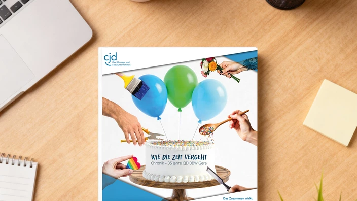 Auf einem Schreibtisch liegt eine Broschüre mit dem Titel "Wie die Zeit vergeht / Chronik – 35 Jahre CJD BBW Gera".