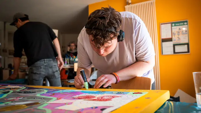 Workshopprojekt - Transzendenz: Eine Person malt mit einem Stift auf ein buntes Kunstobjekt